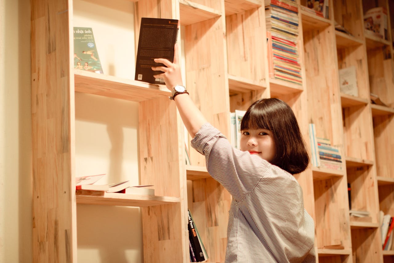 A smiling woman reaches for a book on custom wooden shelves in a cozy library.